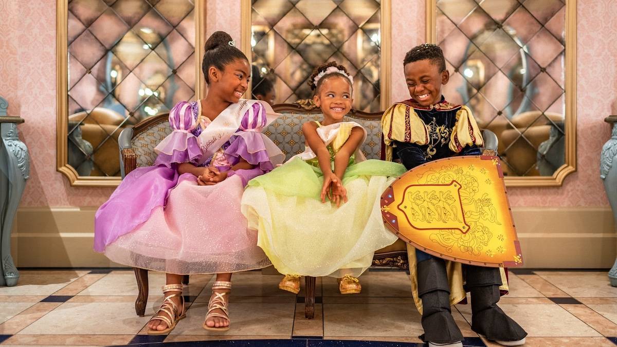 Three kids on a bench, two in princess dresses and one in a knights outfit.